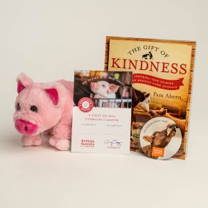 Plush pig and symbolic adoption certificate, 'The Gift of Kindness' book, and a magnet with a hand patting a cows nose and the phrase 'I'm creating a kinder world'